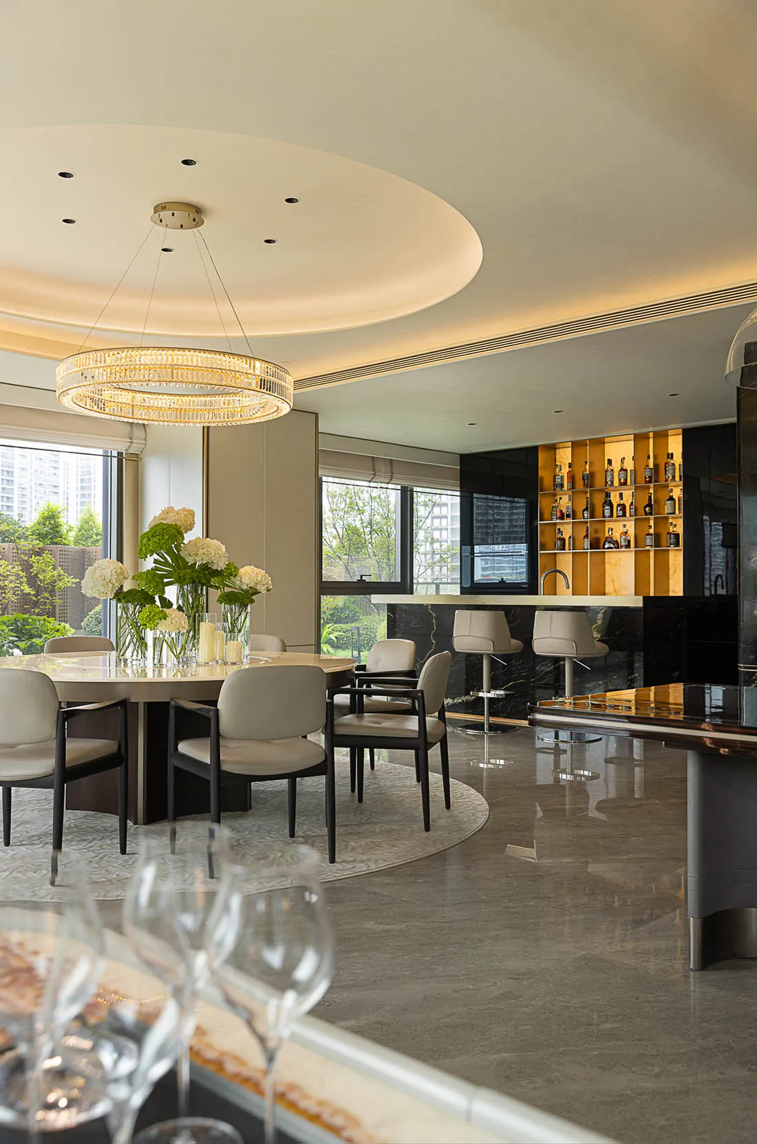 Modern residential dining room featuring marble flooring, seating, and a circular chandelier with flower arrangements on the