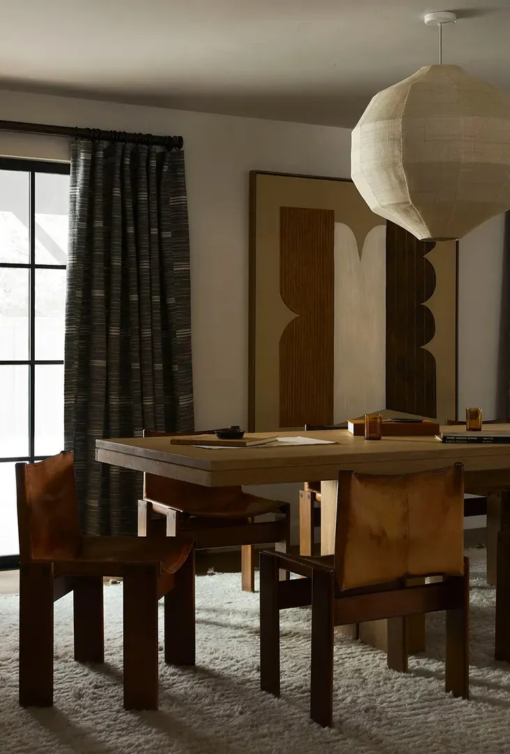 Modern dining room featuring a wooden table with leather chairs, a large abstract artwork, and a textured fabric lampshade.