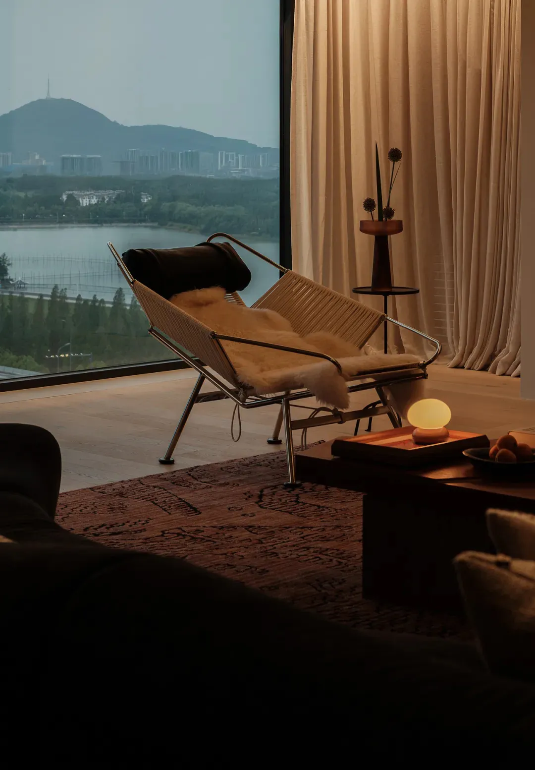 Contemporary armchair with wooden frame and faux fur blanket, situated in a modern living room with a cityscape view.