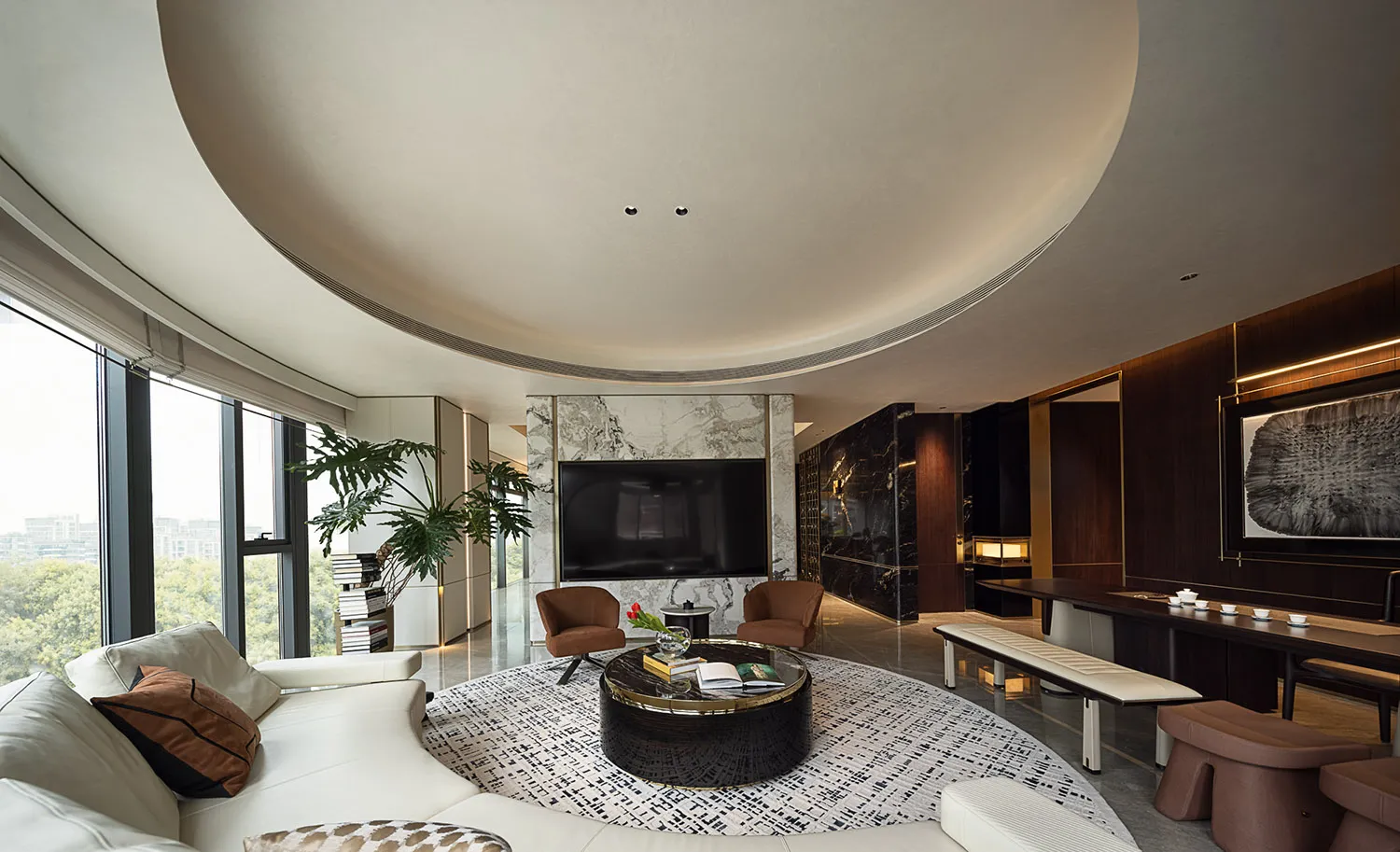 Modern living room with a large white sofa, round black coffee table, large windows, and marble accents.