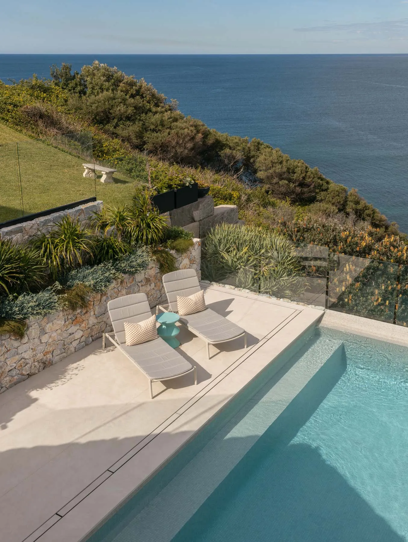 Modern pool deck with concrete patio, lounge chairs, and sea view.