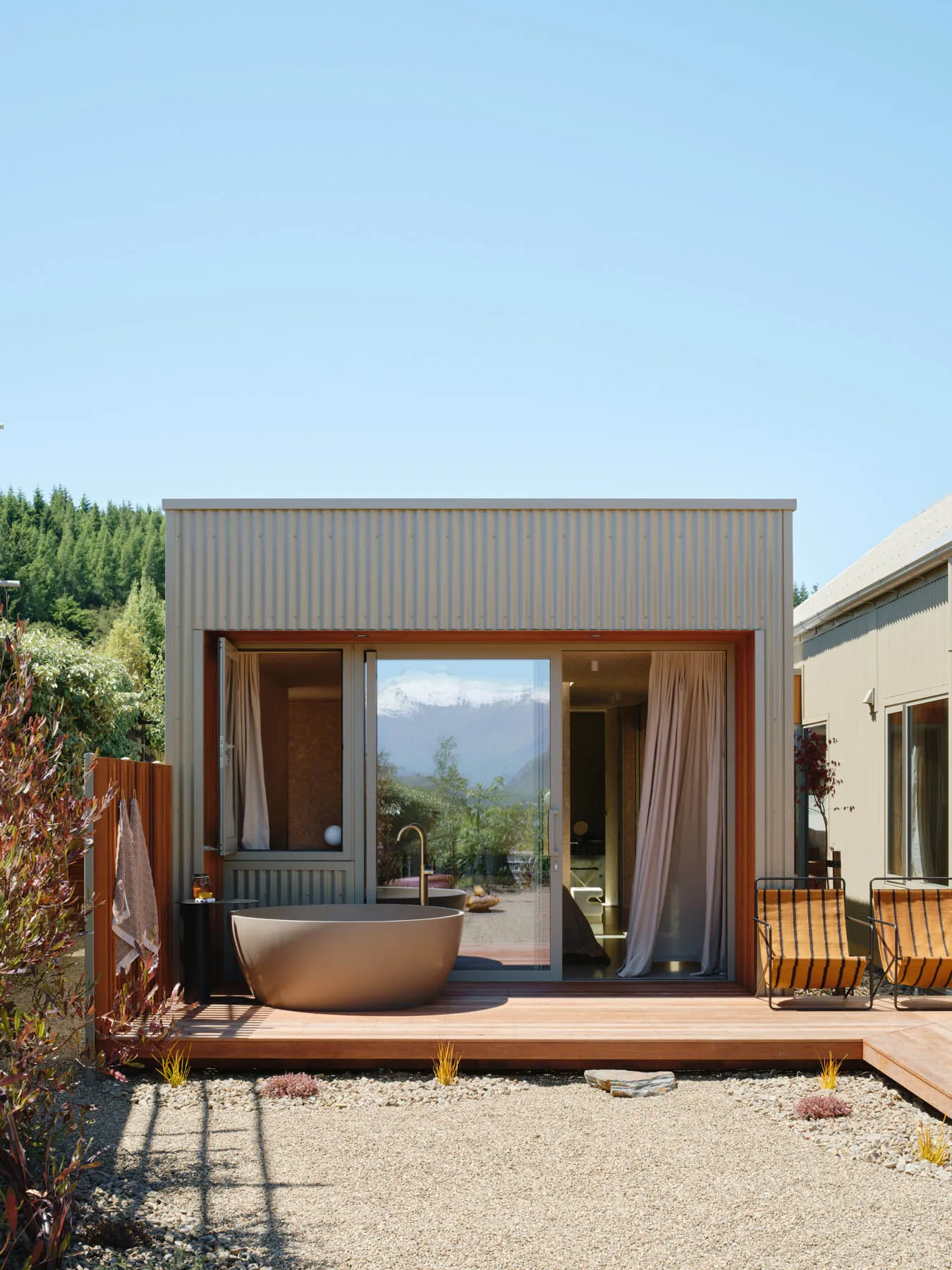 An industrial-style bathroom with a metal bathtub, glass doors, and corrugated metal walls.
