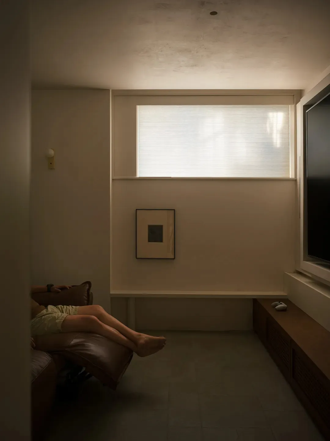 A minimalist living room featuring neutral-toned furniture and a large television.
