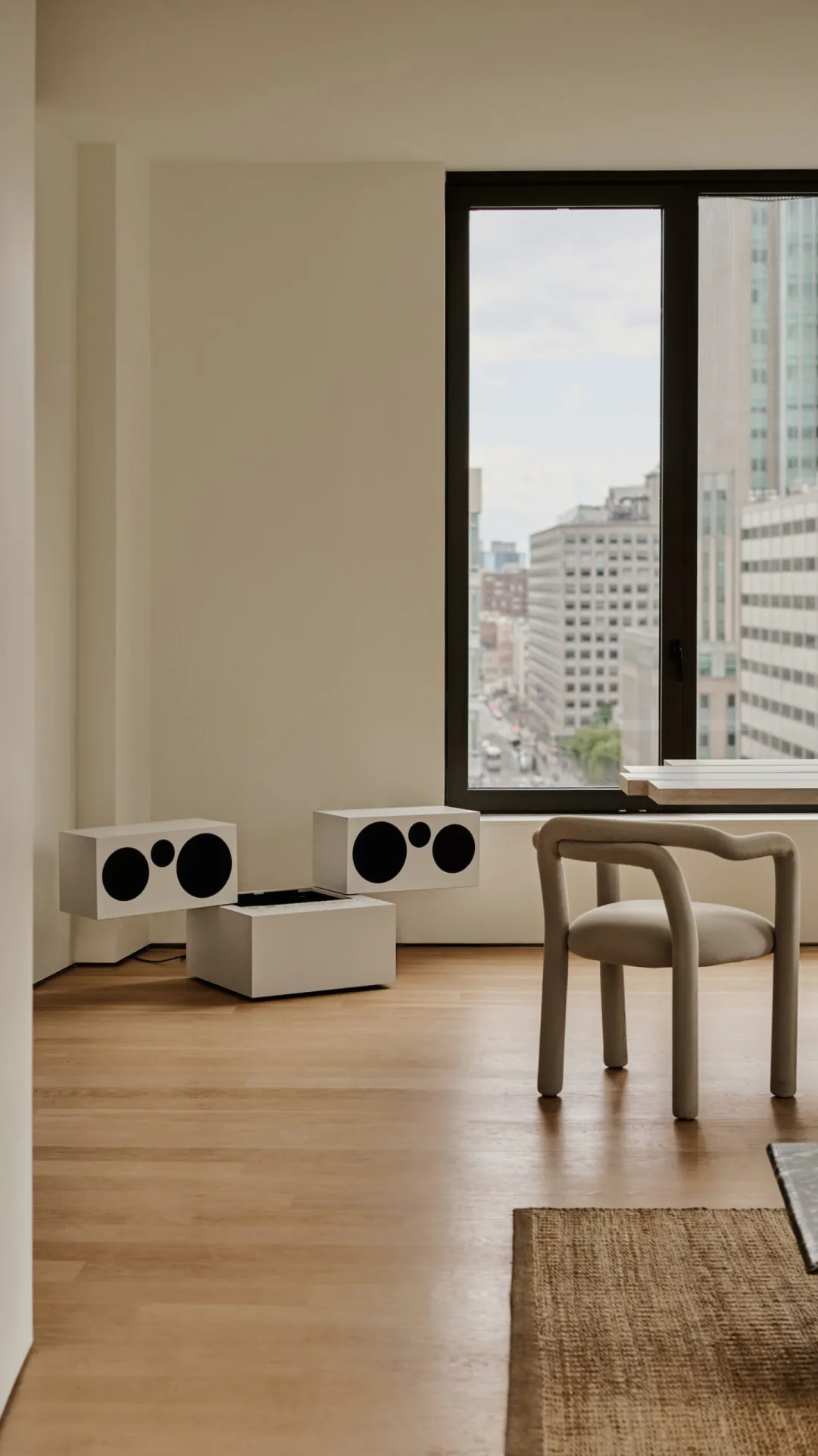 Minimalist living room with wood flooring, a beige armchair, and modern audio speakers.