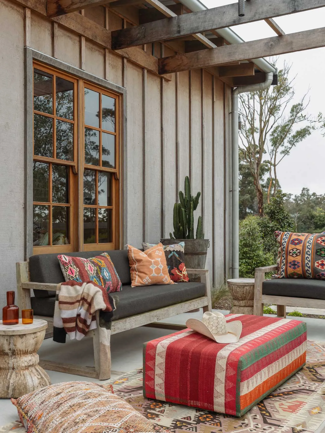 Rustic outdoor living space featuring wooden furniture, fabric cushions, concrete flooring, and metal accents.