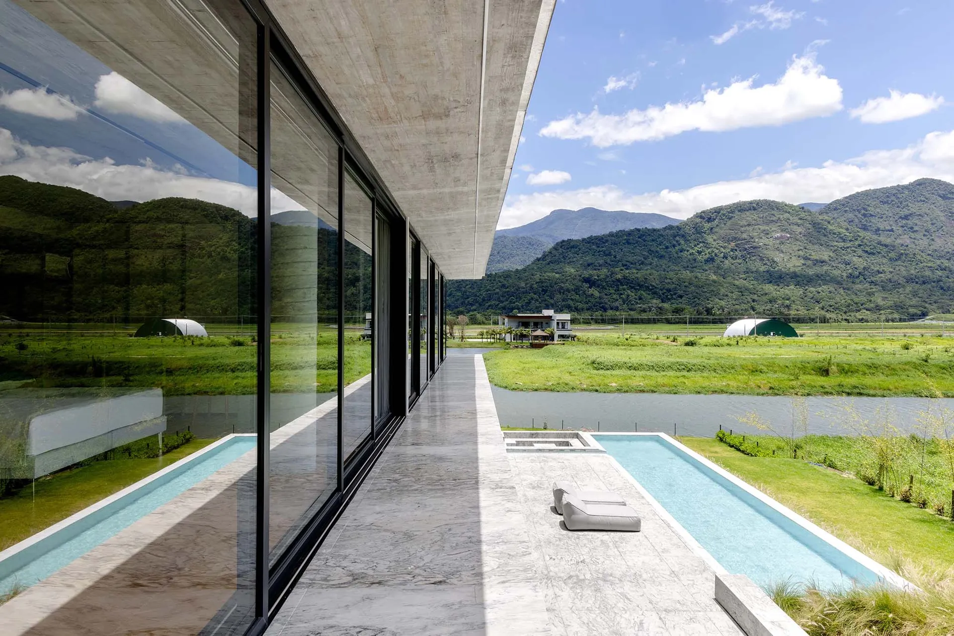 Modern residential house featuring sleek concrete and glass architecture with a poolside view of green fields and mountains i