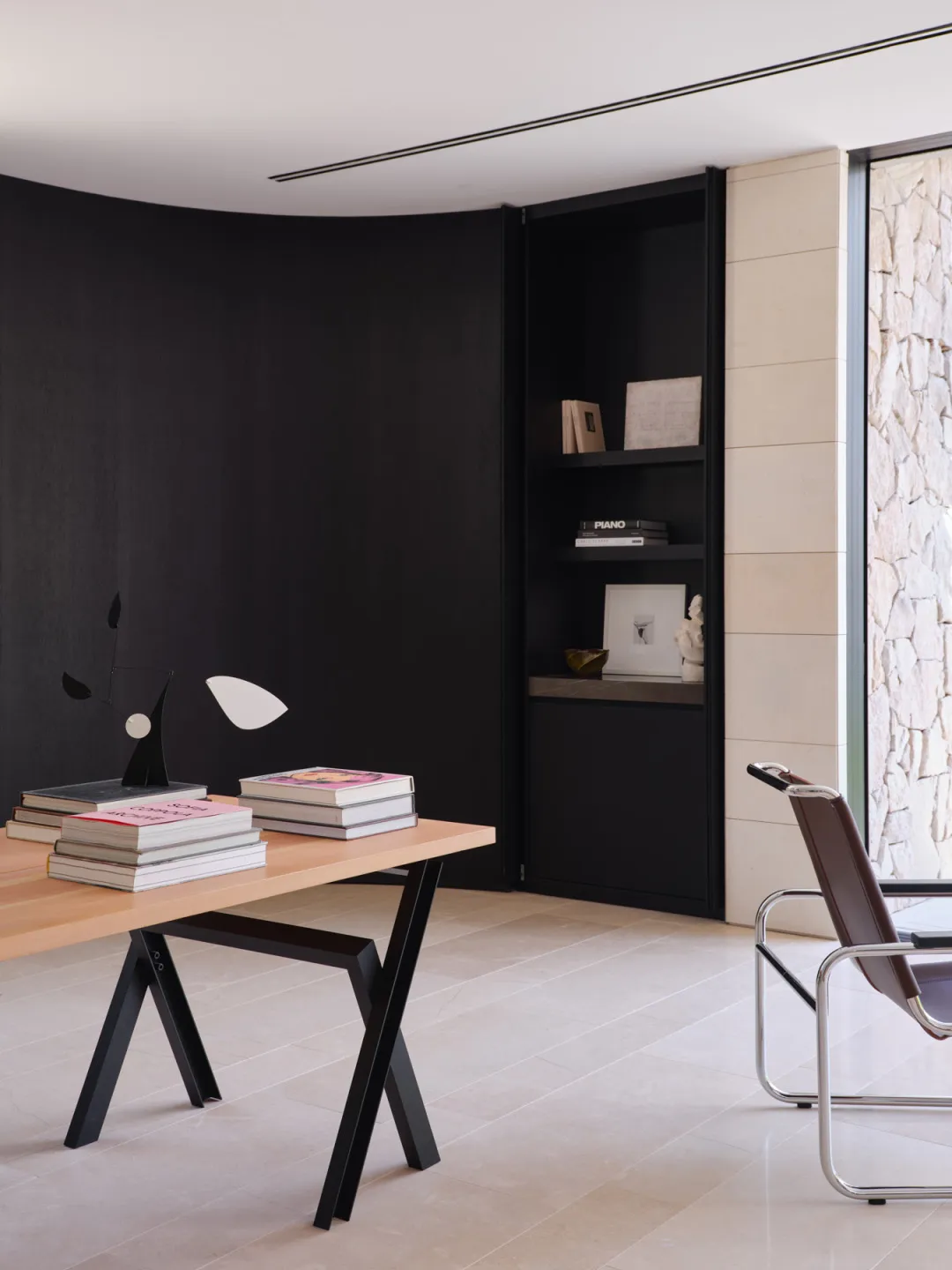 A modern, minimalist home office featuring a black metal and wood desk with books and a lamp, alongside a sleek, minimalist a