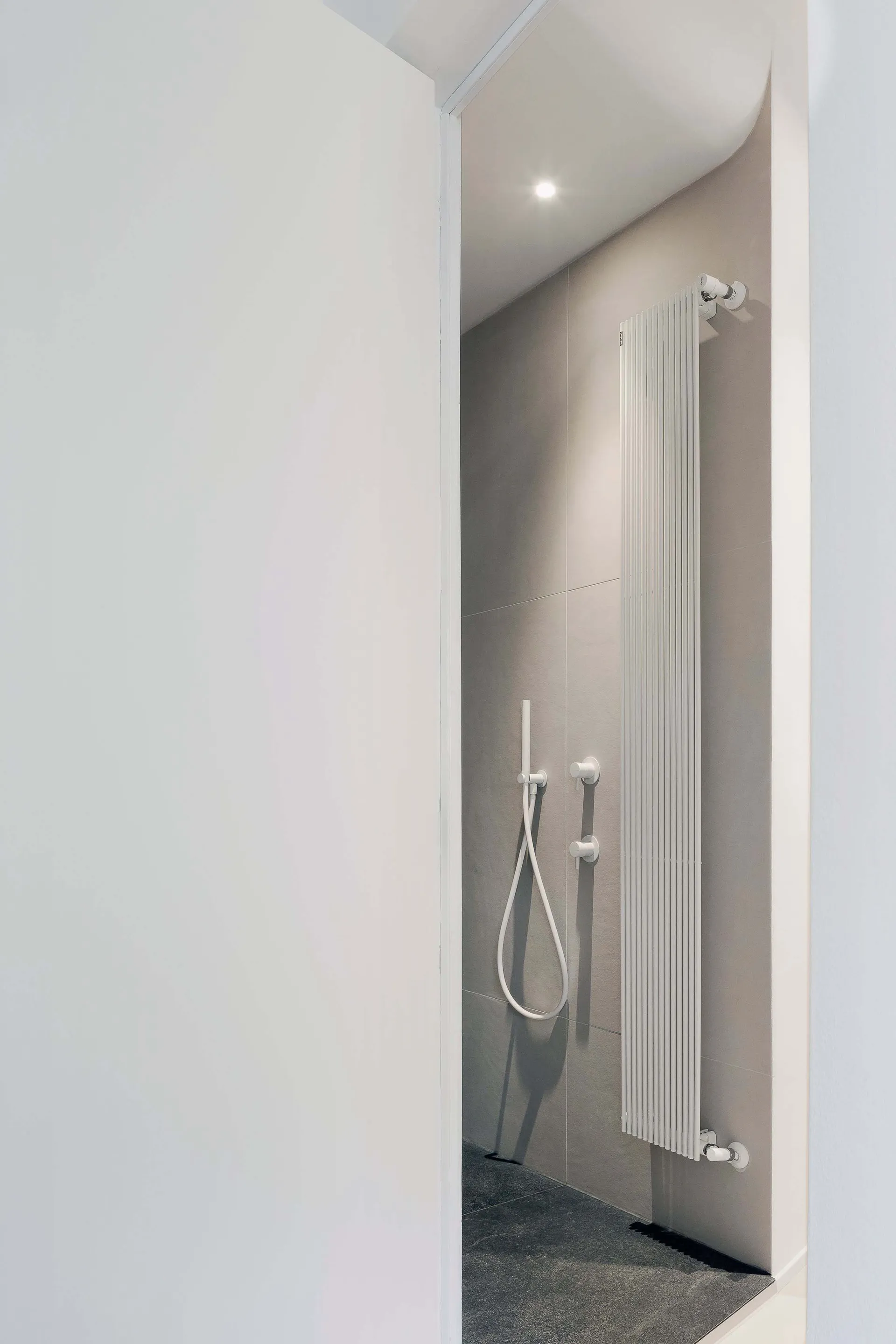Modern minimalist bathroom featuring ceramic tiles flooring and walls, with a sleek white radiator and simple fixtures.