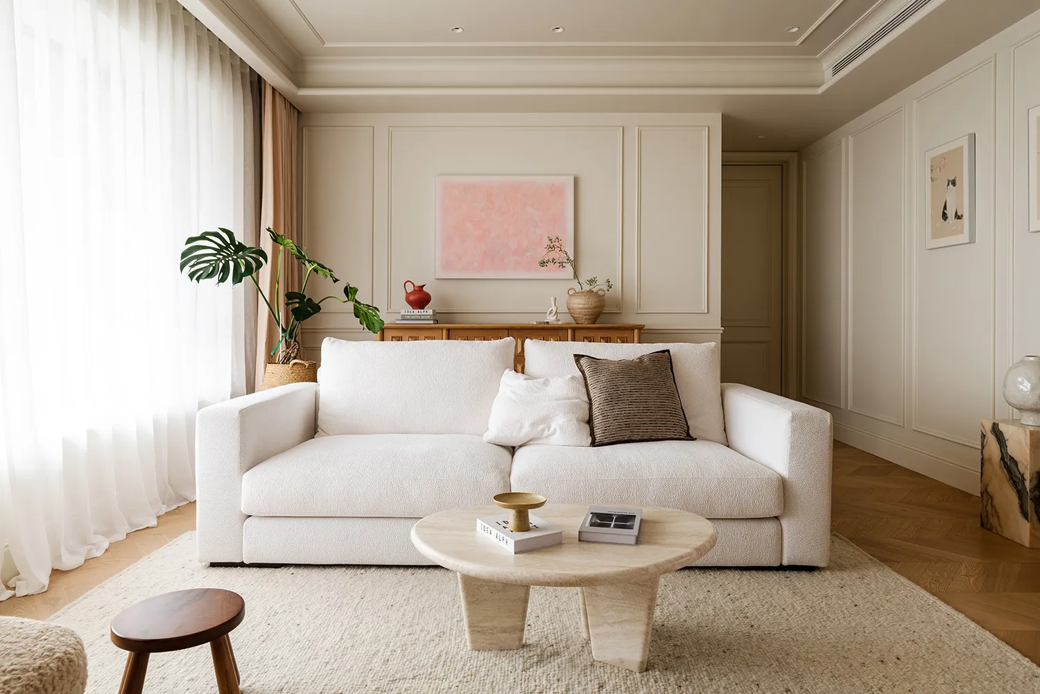 A minimalistic living room with a white couch, neutral-toned rugs, and a round coffee table.