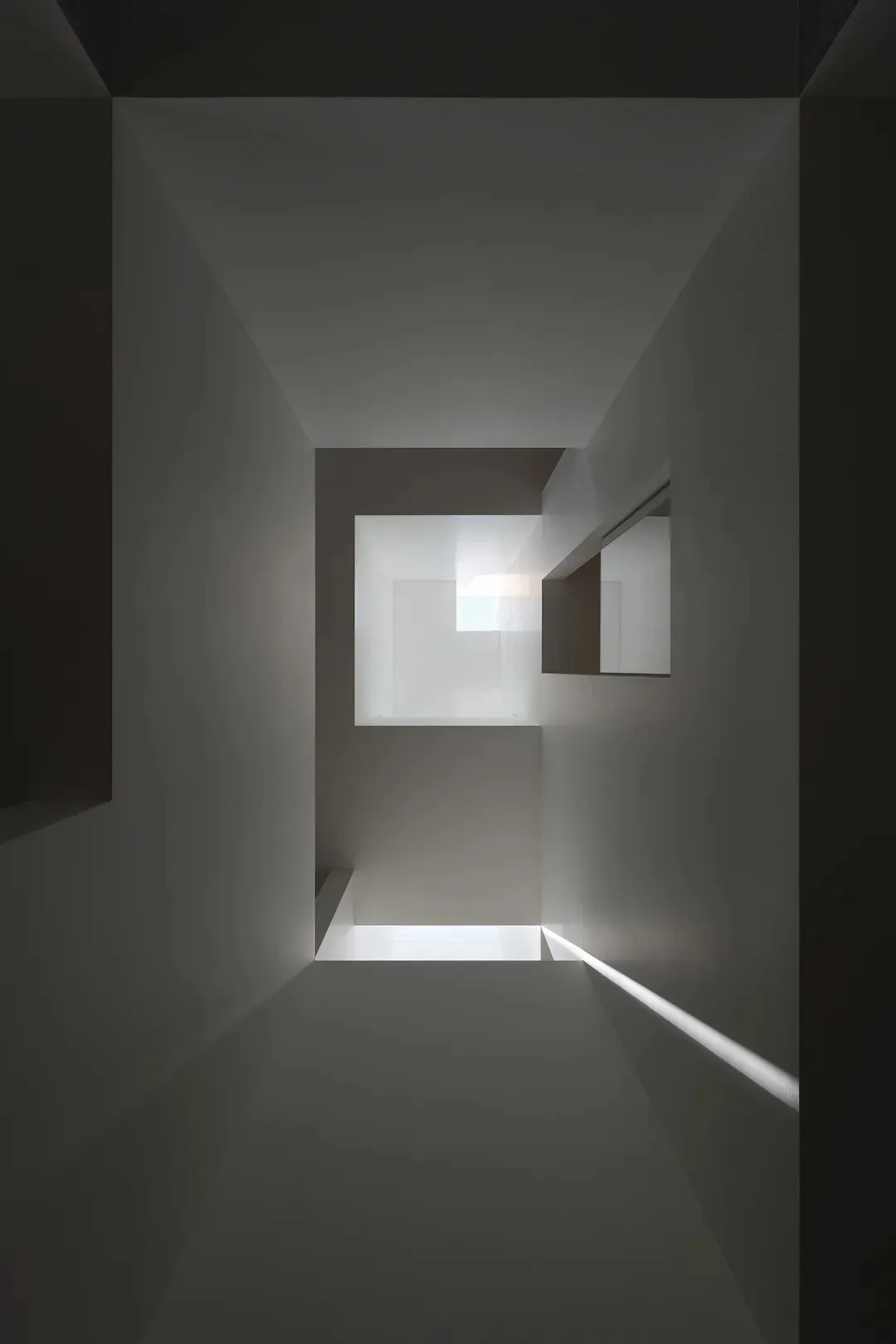 An minimalist white concrete corridor with a skylight letting in natural light.