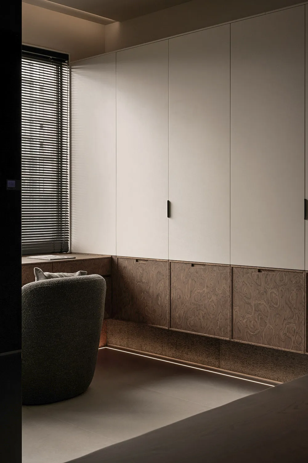 A modern minimalist bedroom featuring a sleek storage system with light and dark wood finishes, and a comfortable upholstered