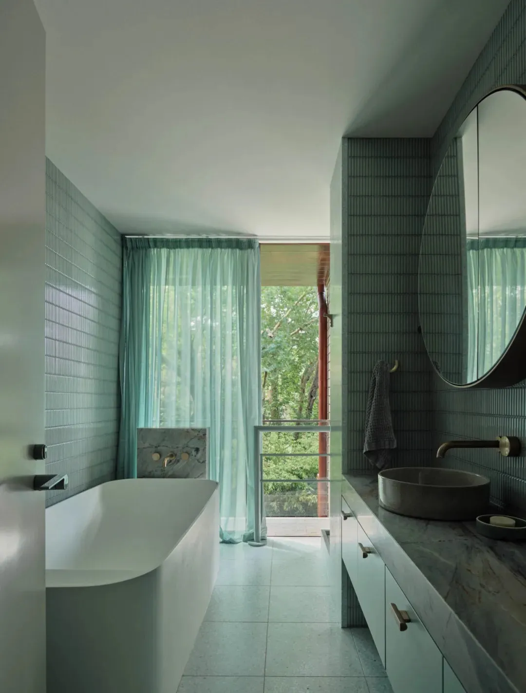Modern minimalist bathroom featuring ceramic tiles, a stand-alone bathtub, and a floating vanity with a round mirror and a ve