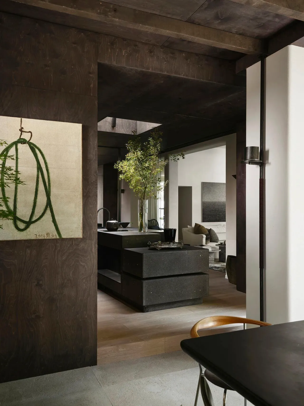 A modern industrial residential interior featuring a concrete kitchen island and wooden dining table with a dark wood floor.