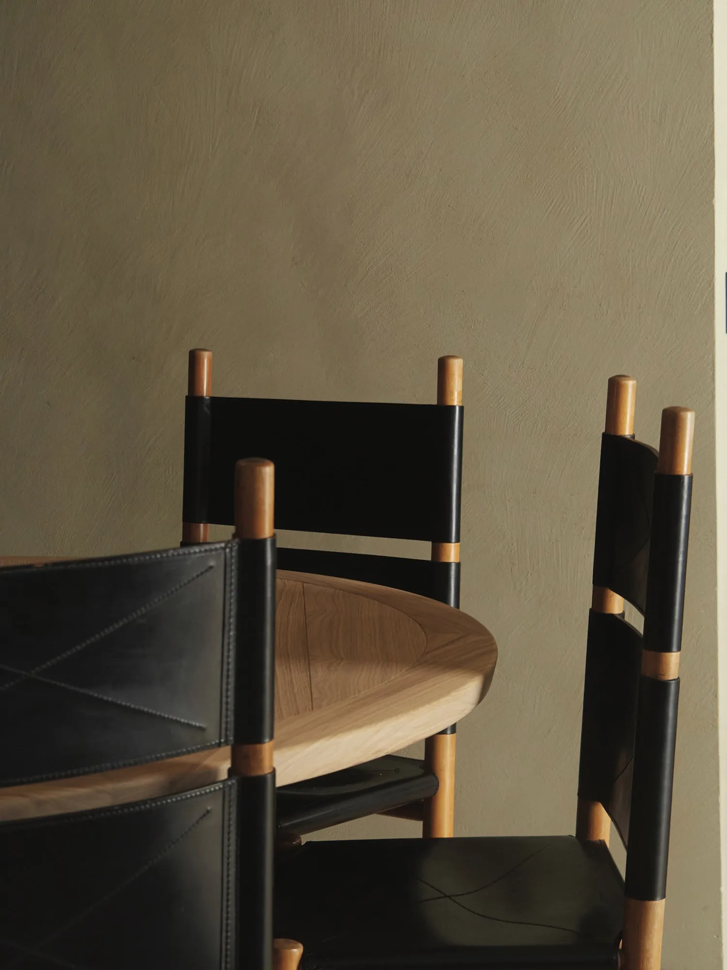 A modern interior design featuring wooden chairs with black leather seating and backrests.