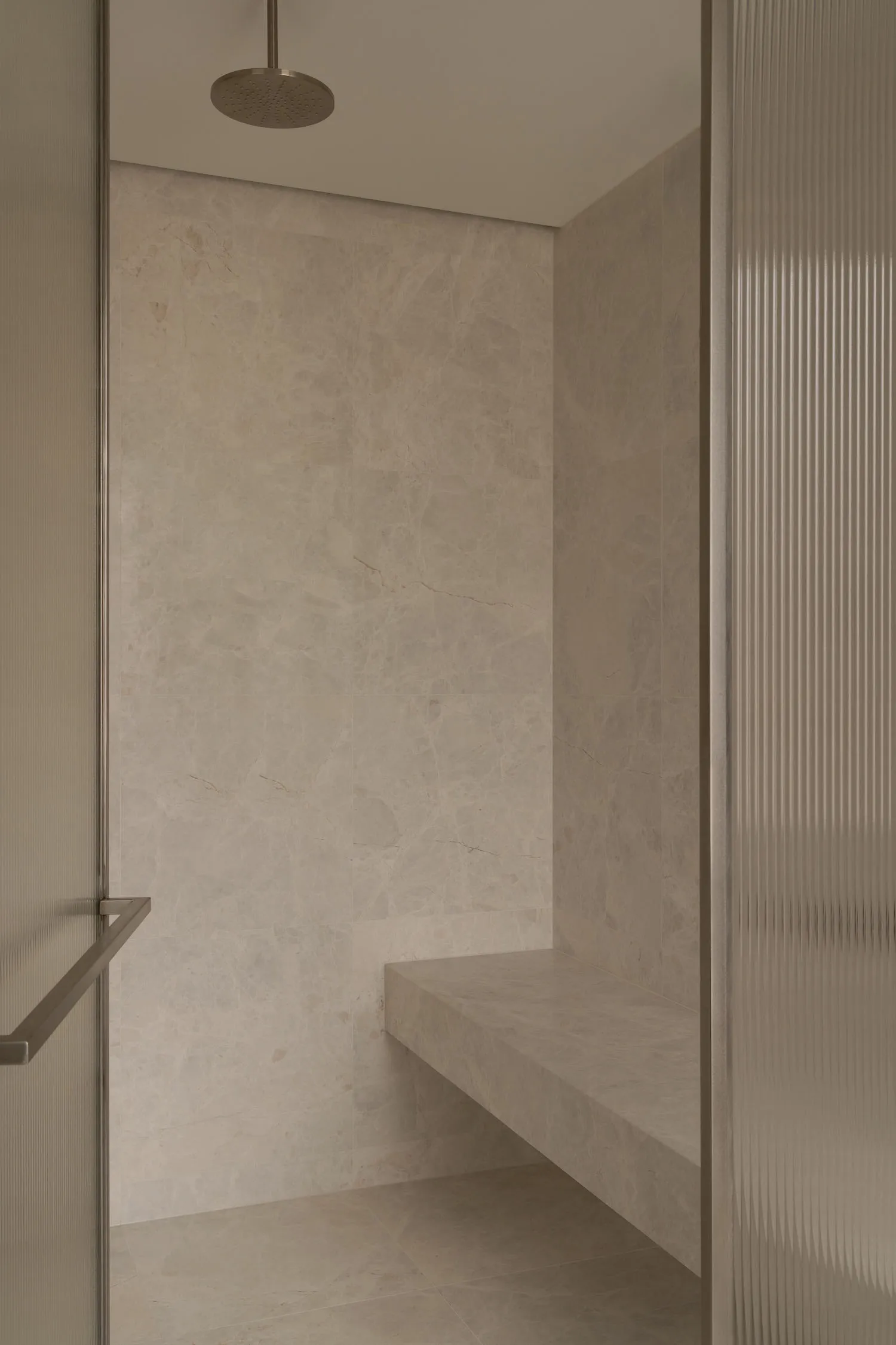 A minimalist bathroom with marble walls and floor, featuring a shower with a built-in bench seat.