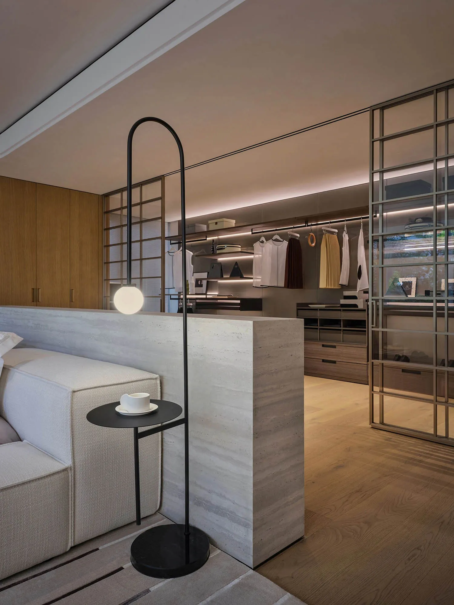 A modern bedroom featuring a bed with a white headboard, a side table with a black lamp and a cup of coffee, and a closet wit