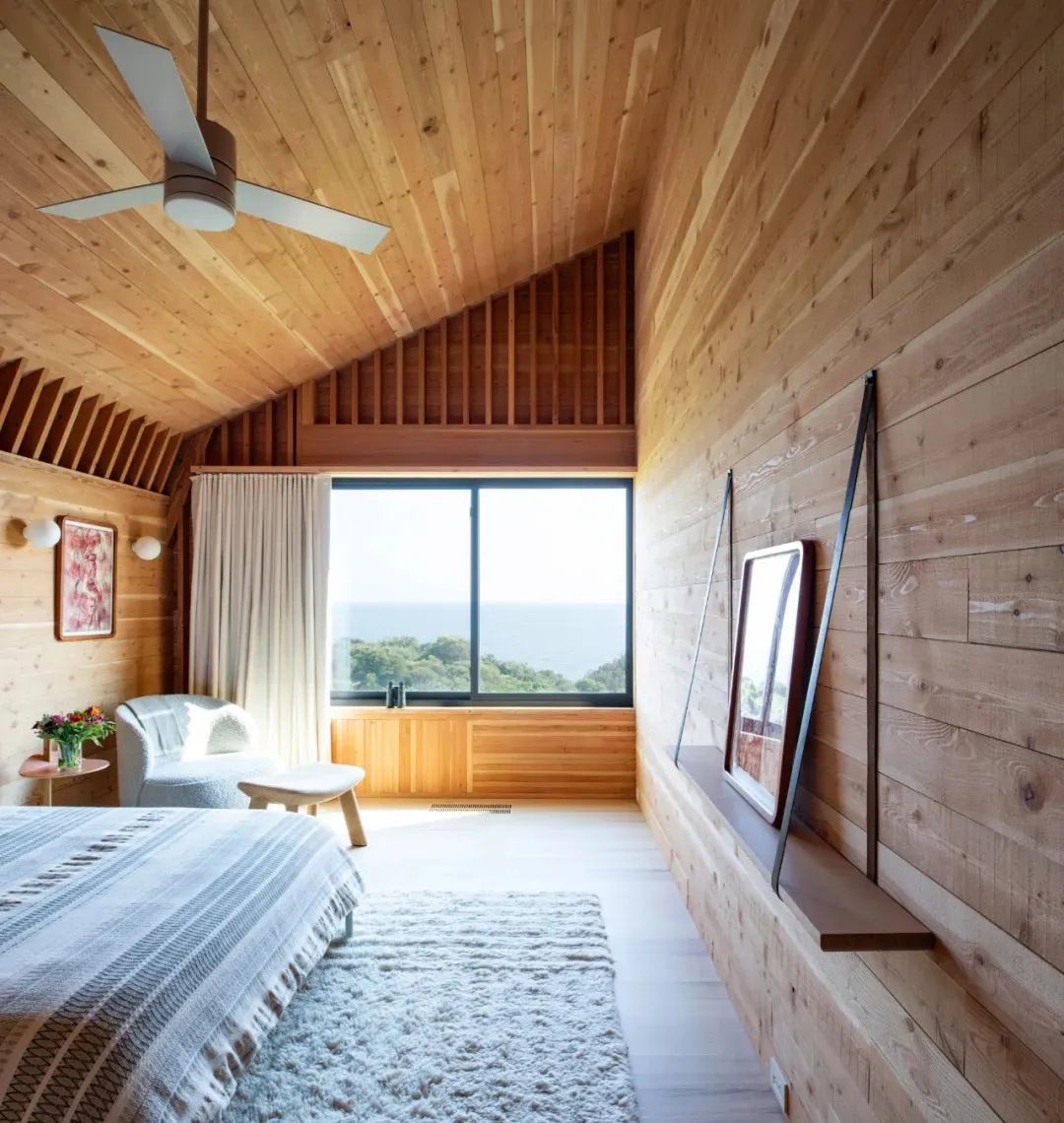 A minimalist bedroom featuring wood paneling, a large window with a view, and a cozy seating area.
