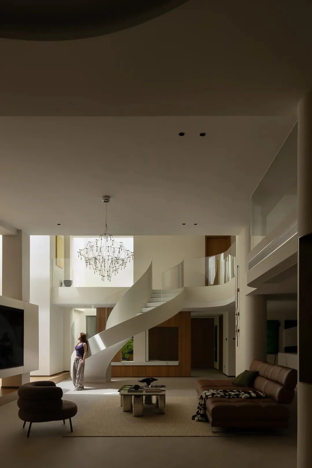 A modern minimalist living room featuring a white staircase, pendant chandelier, and minimalist furniture.