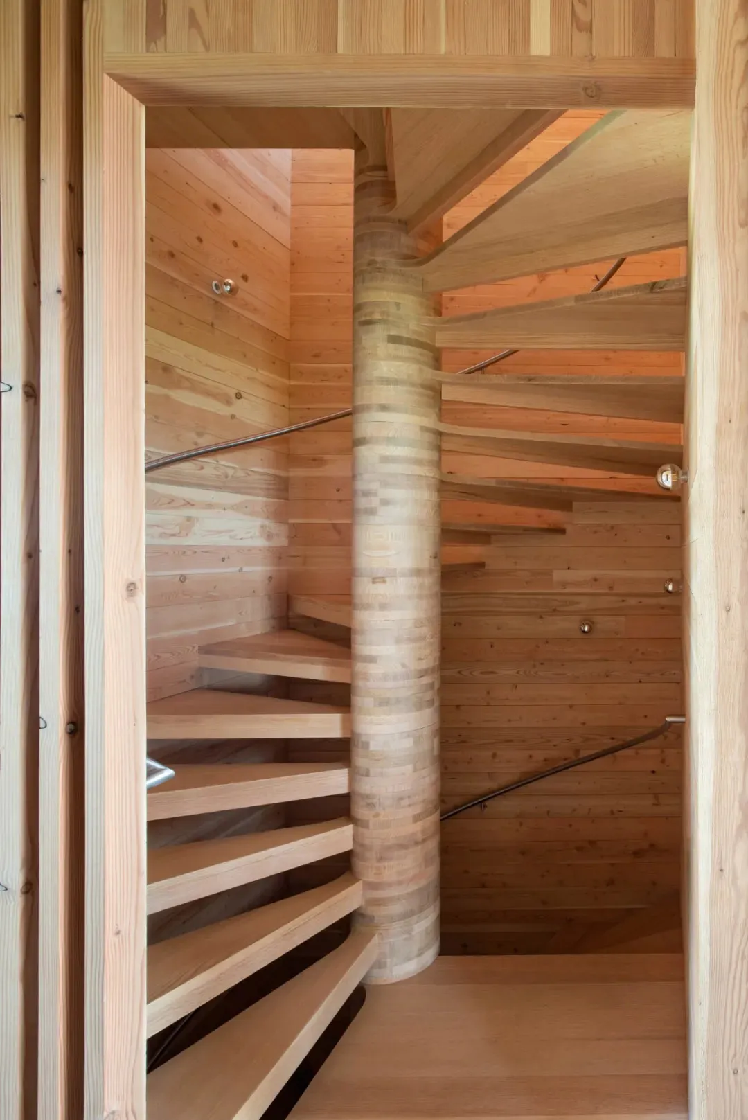 A modern, spiral staircase with wooden steps and railings inside a wooden building.