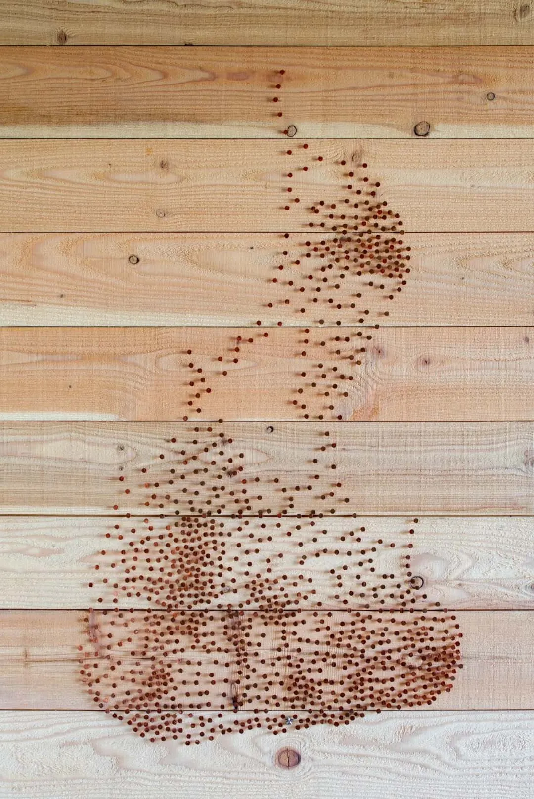 A piece of industrial-style string art made from wooden beads arranged on a wooden surface to form the shape of a coffee cup
