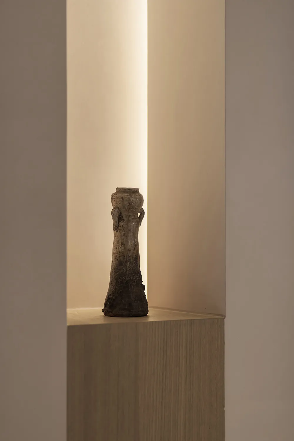 A ceramic vase with an industrial style design sits on a wooden pedestal in a minimalist setting.