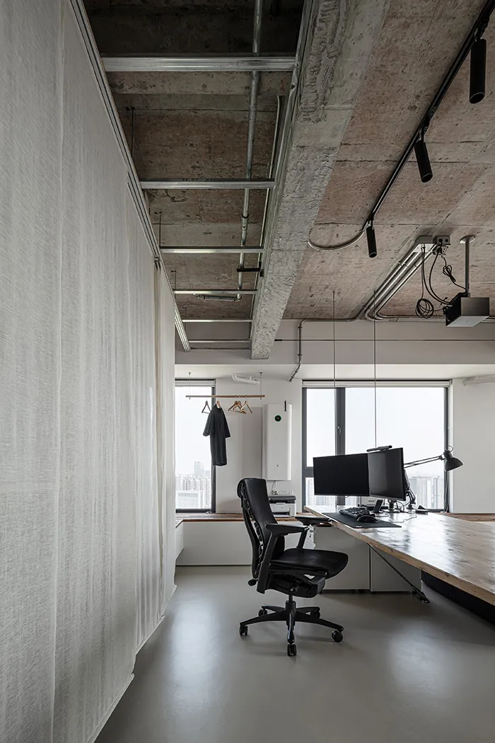 A modern industrial-style workstation with a concrete desk, black office chair, and minimalistic design elements.