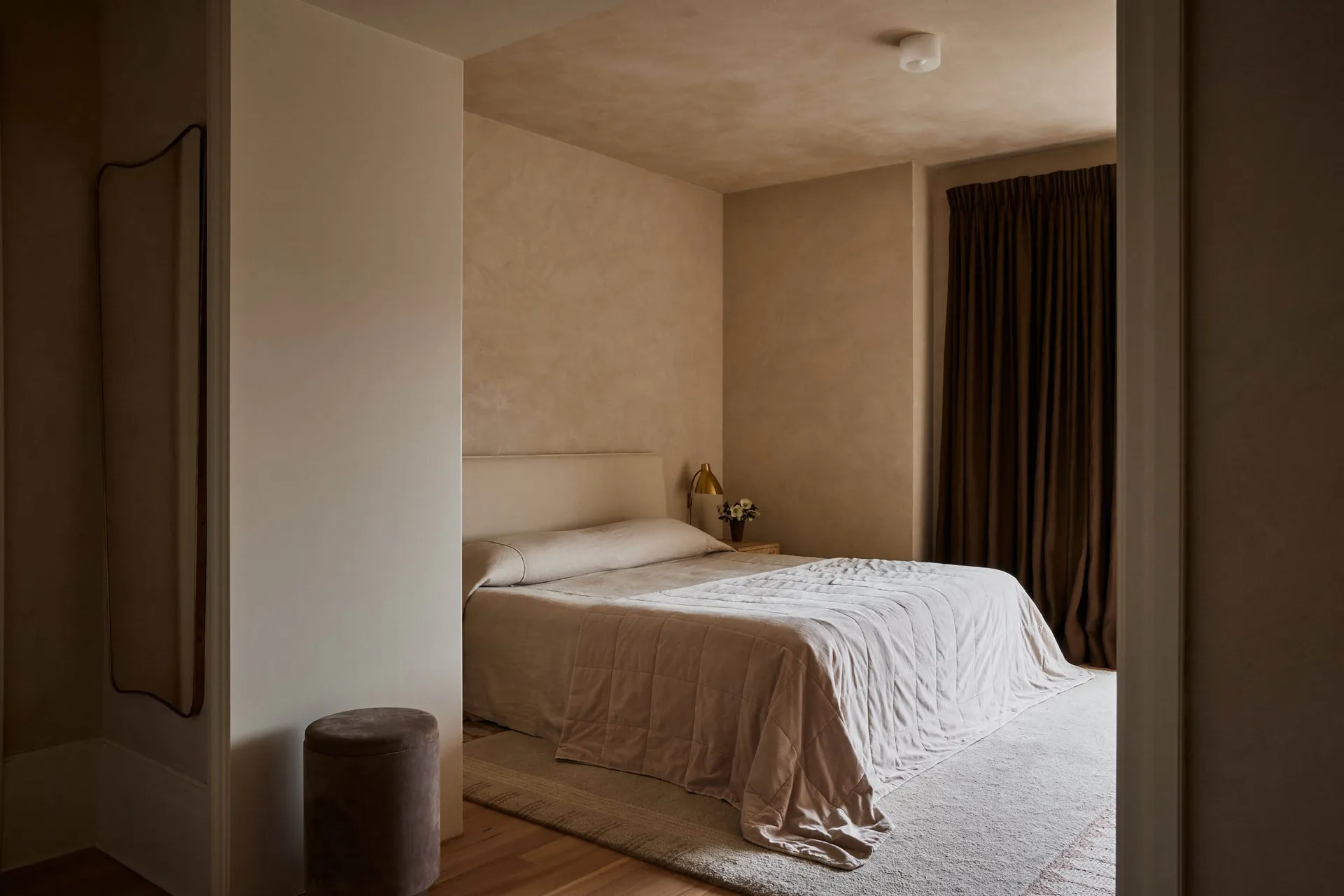 A minimalist bedroom with light brown fabric textiles on a neatly made bed.