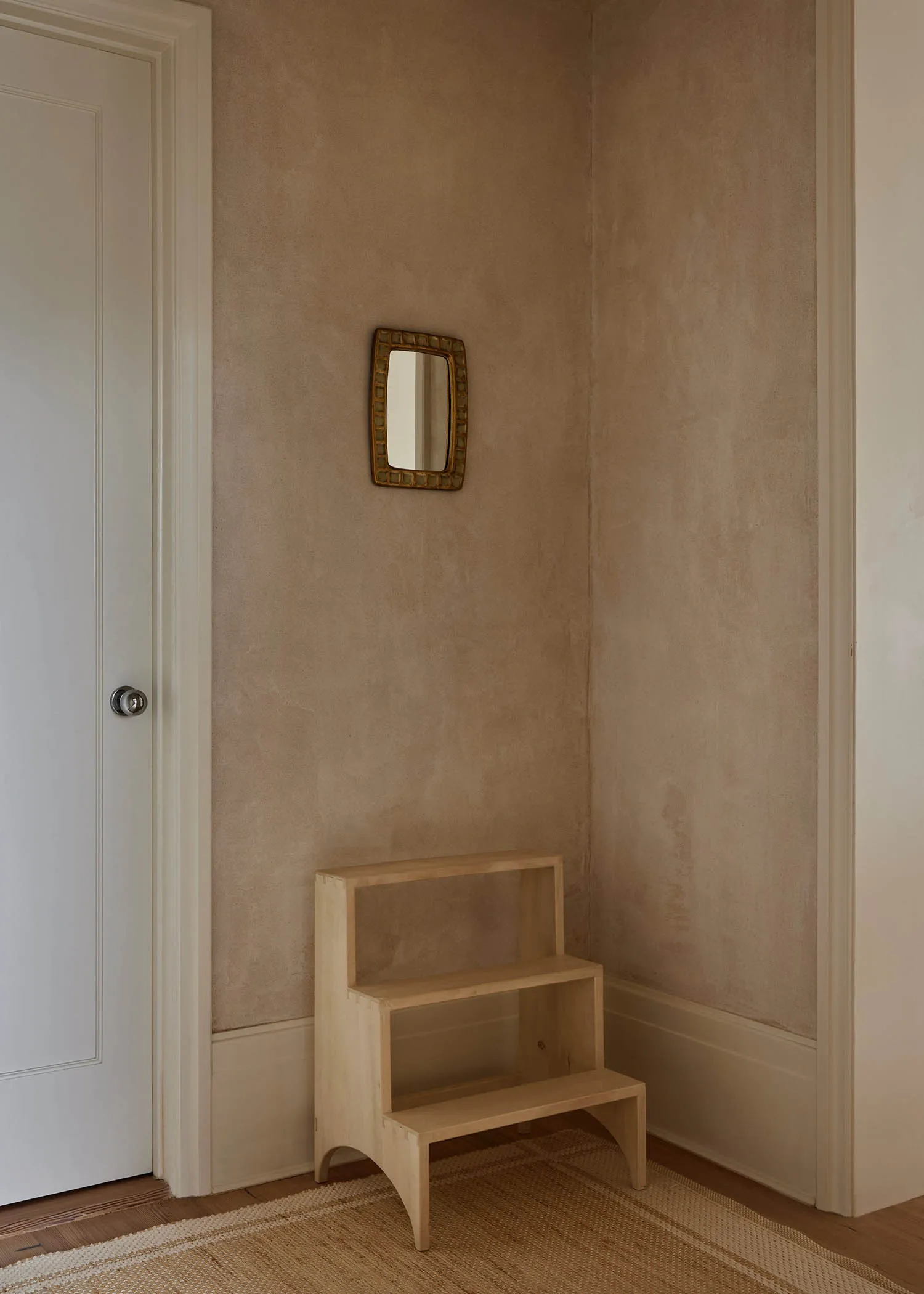 Minimalist interior design featuring a wooden shelf with a small mirror on the wall and a white door.