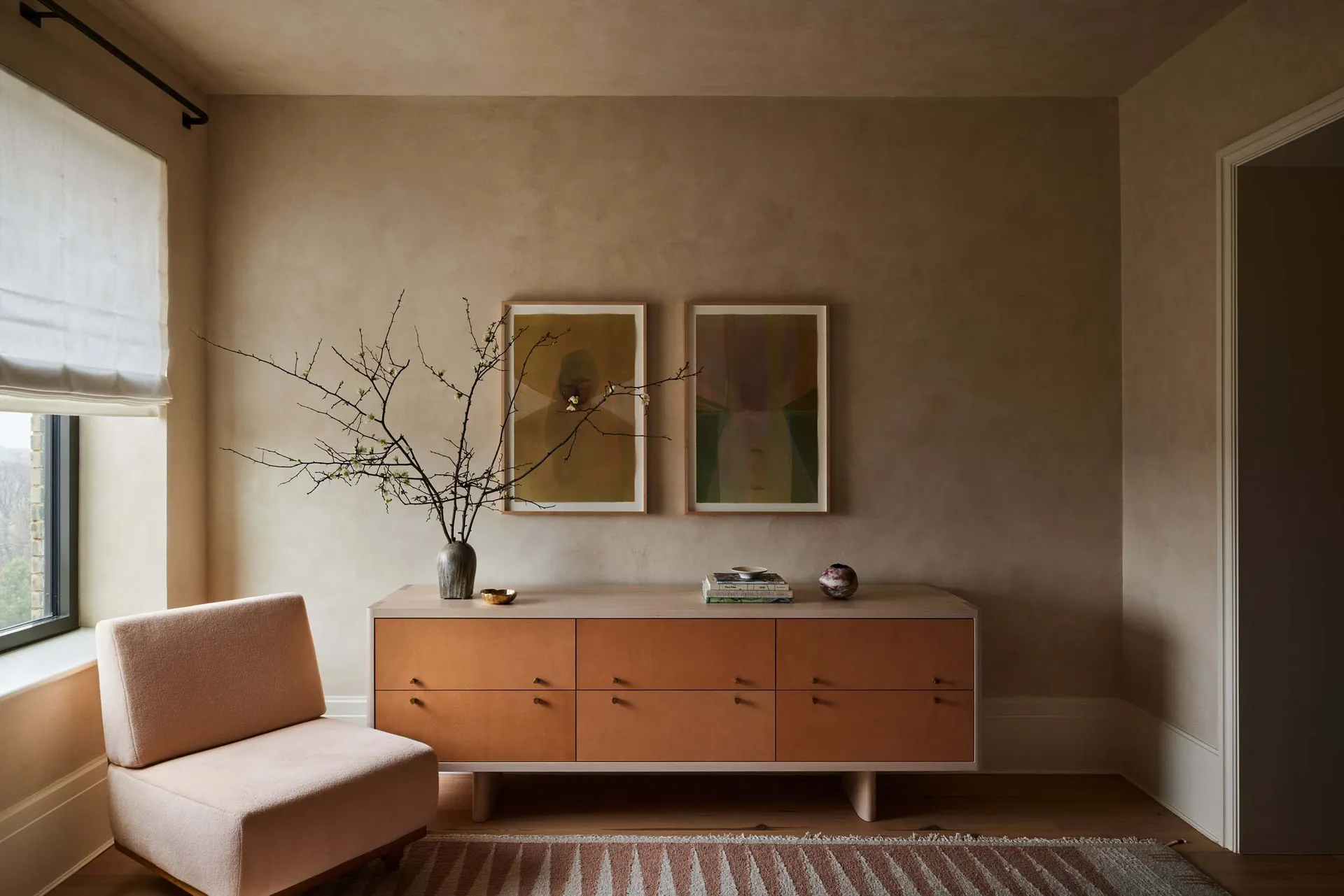 Minimalist residential room featuring concrete surfaces, a pink armchair, and a wooden cabinet.