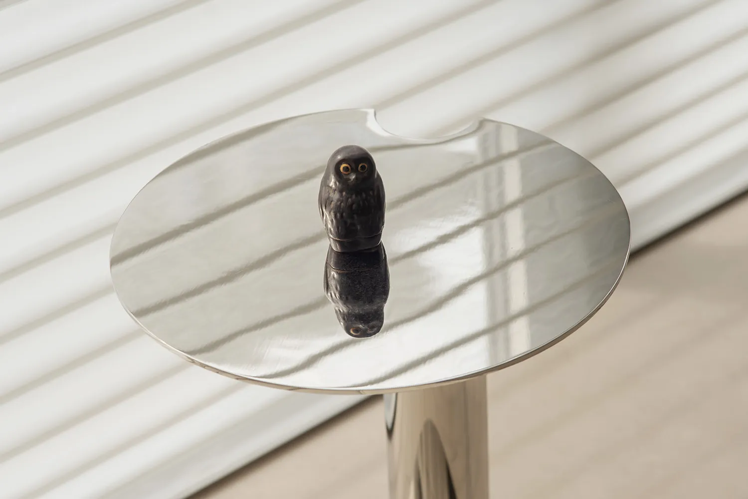 A modern metal sculpture depicting an owl on a reflective tabletop.