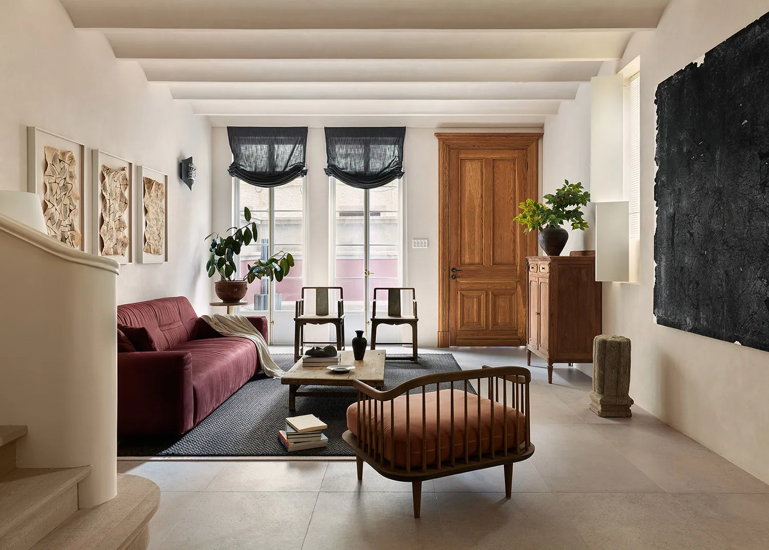 A modern living room featuring a burgundy sofa, wooden armchairs, and a wooden coffee table.
