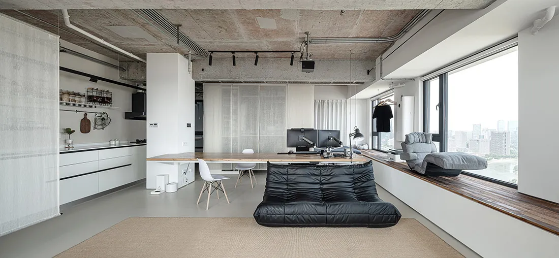 A modern living/office space featuring concrete floors, white walls, and a wooden desk.