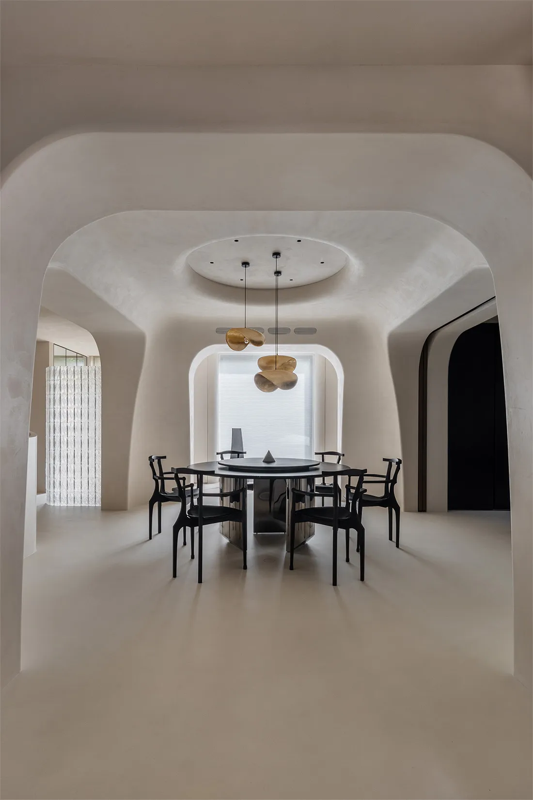 A minimalist dining room with round concrete floor, black chairs, a round table, and abstract lighting fixtures.