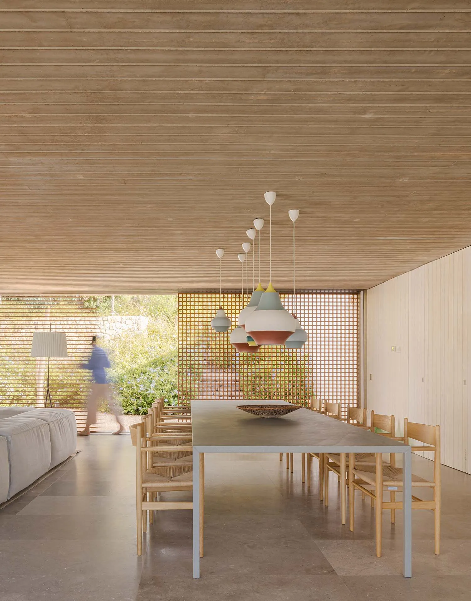 Modern minimalist dining room featuring wooden furniture, concrete floor, and colorful pendant lights.