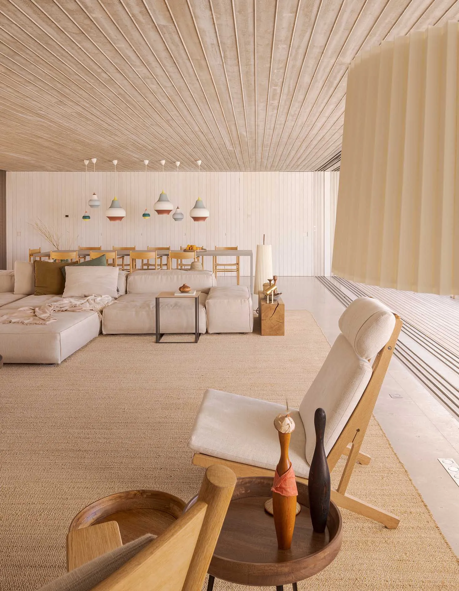 A modern living room featuring neutral-toned furniture, a wooden floor, and a ceiling with linear wood paneling.