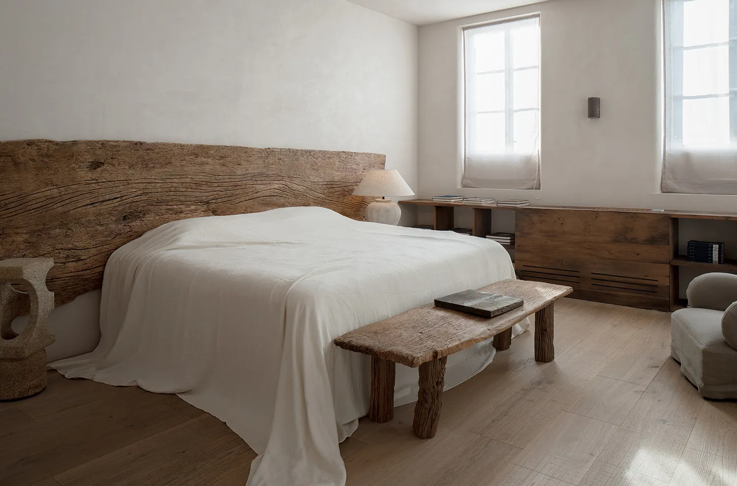 A minimalist bedroom featuring a wooden bed with a textured wooden headboard and a matching wooden bench.