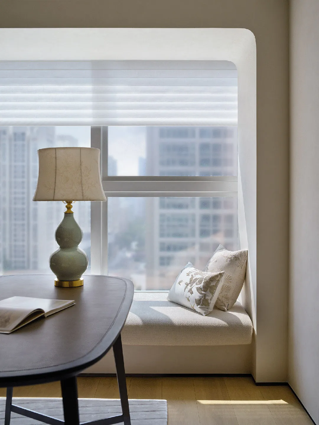 A minimalist home office space with a window seat, an oval table, and a lamp.