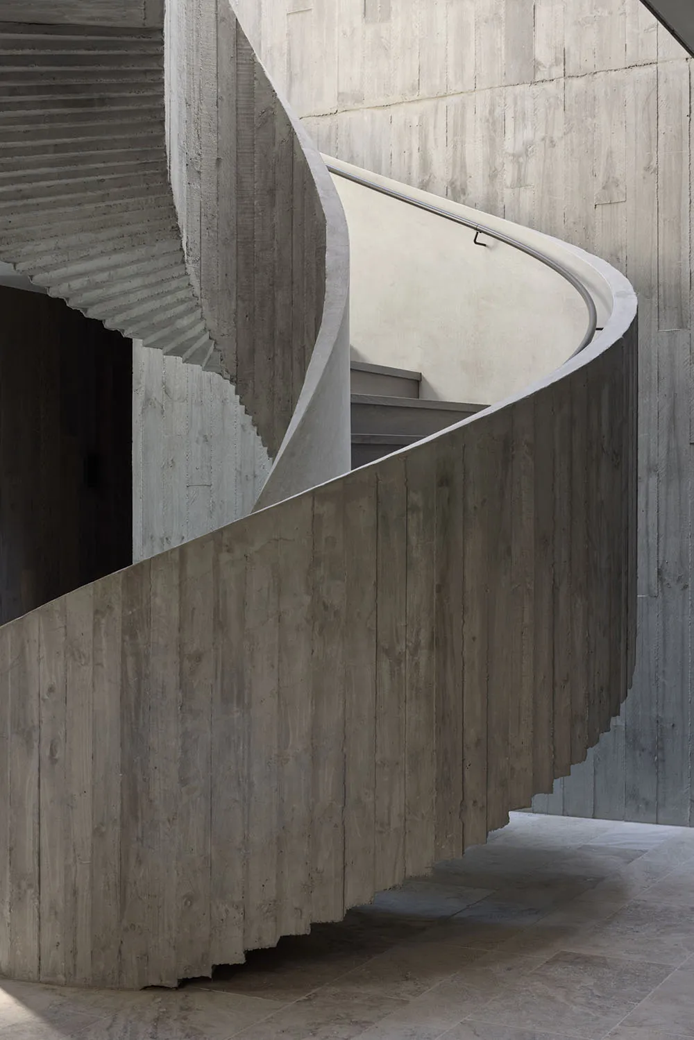 A modern concrete staircase with smooth, curved steps and a handrail.