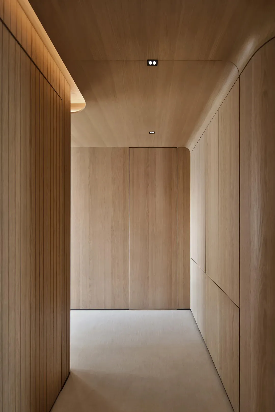 A modern corridor with wooden walls and floors, featuring curved designs and hidden lighting.