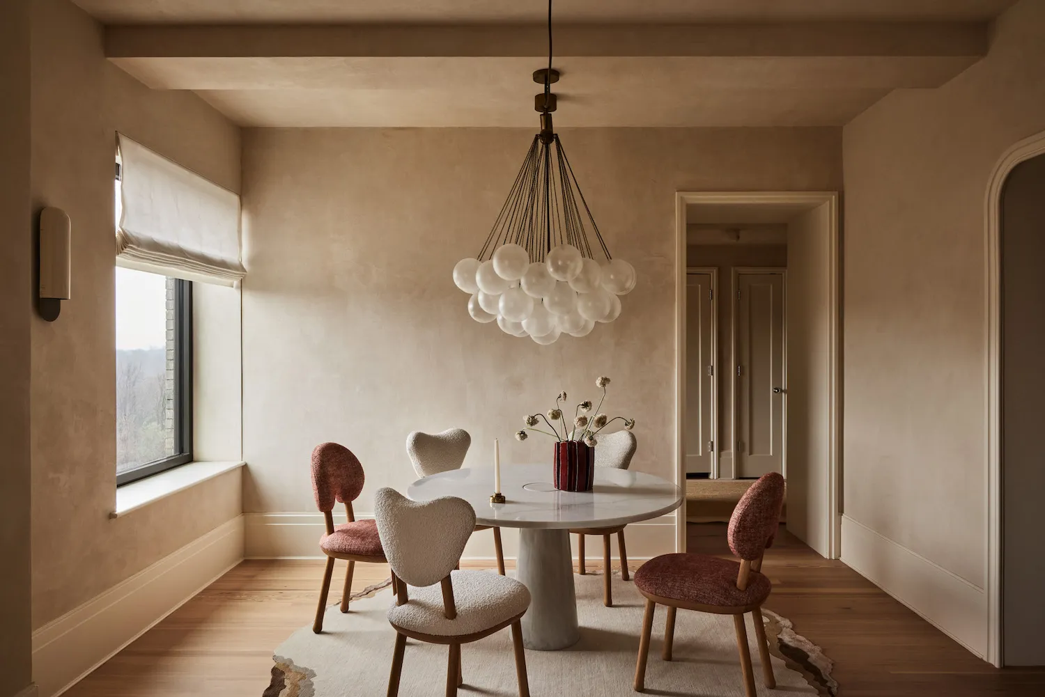 A modern dining room with a marble table, upholstered chairs, and a chandelier with frosted glass globes.