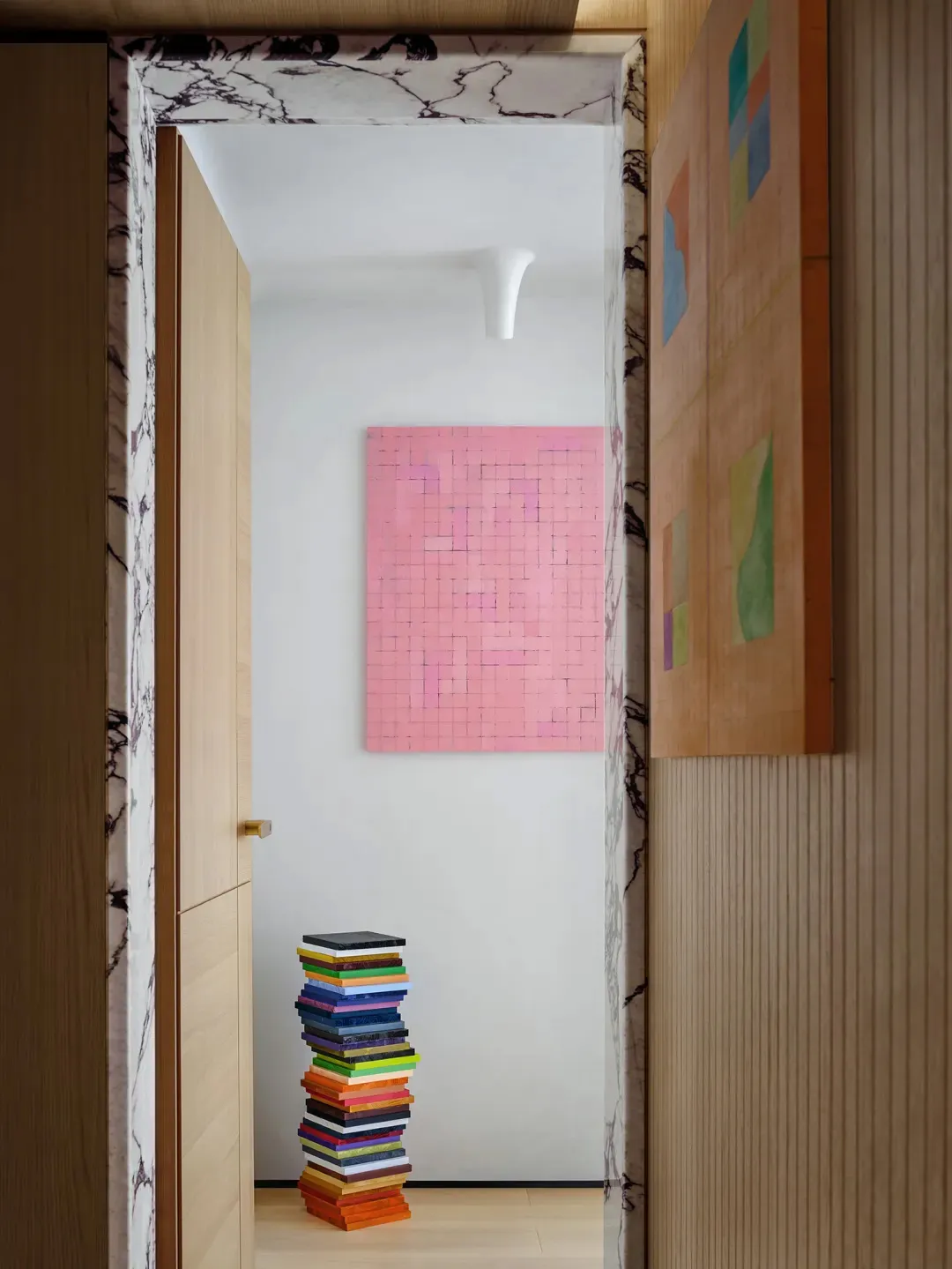 A modern interior hallway with a pink mosaic art piece and a stack of colorful books.