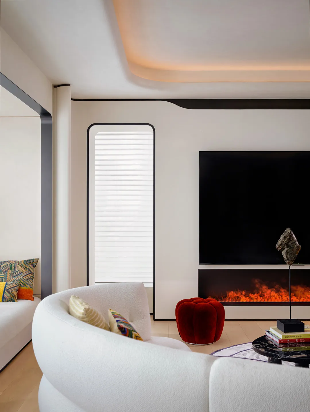 A modern living room featuring concrete walls and floor, with white curvilinear furniture, a red pouf, and a fireplace.