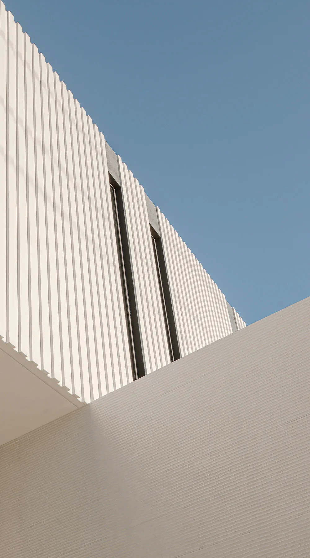 A white, modern metal building with a curved roof and vertical lines against a clear blue sky.