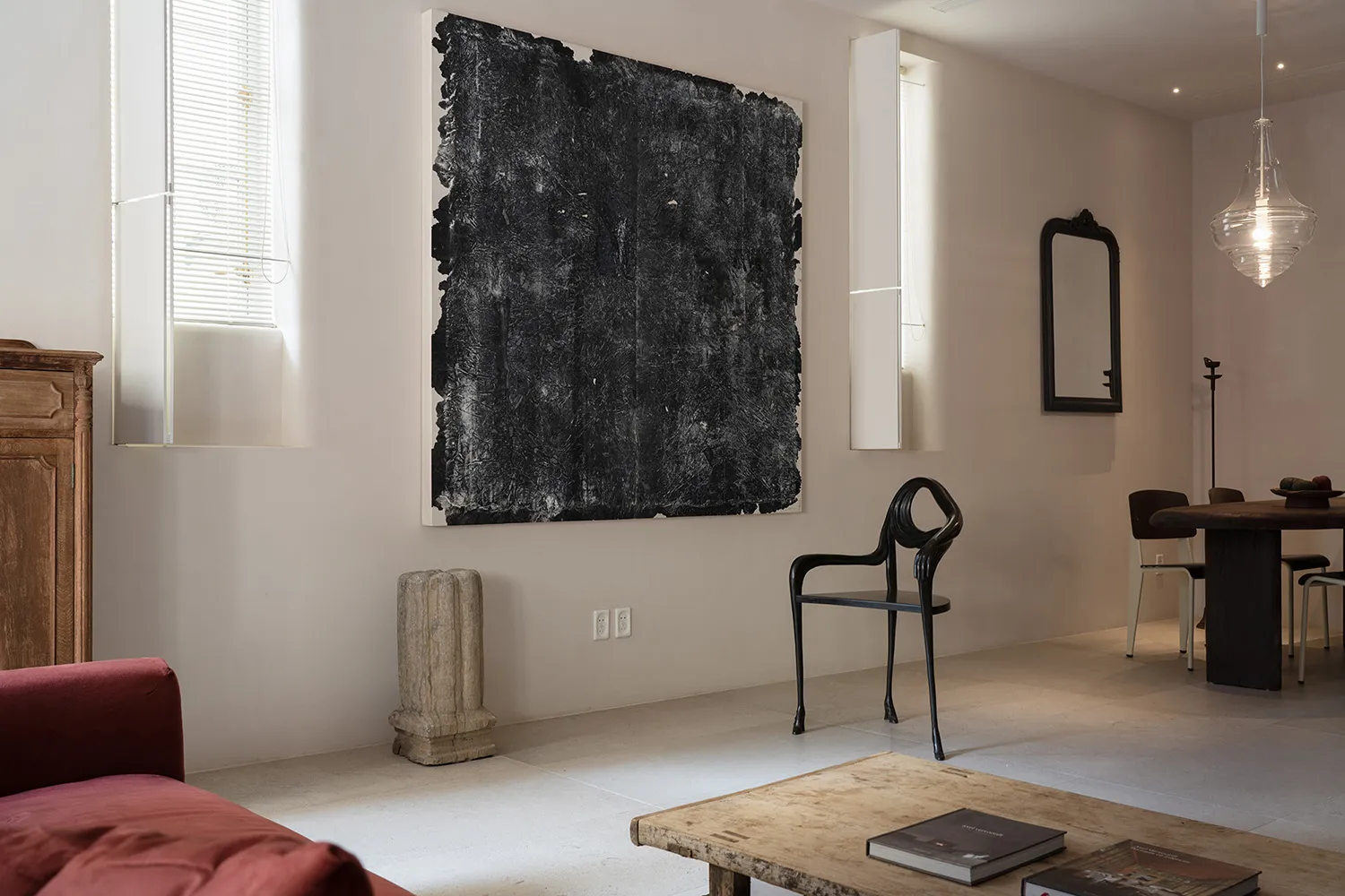 A minimalist living room with a natural wood coffee table, a red sofa, and an abstract black and white painting on the wall.