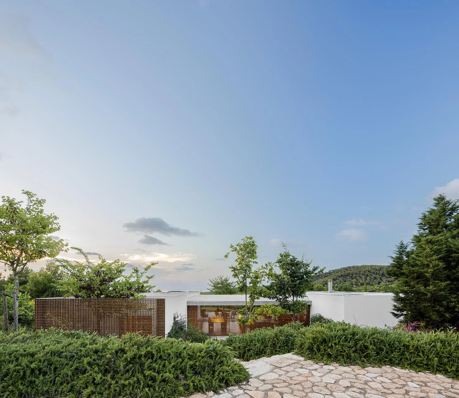 A modern residential architecture with white walls and greenery surrounding the building.
