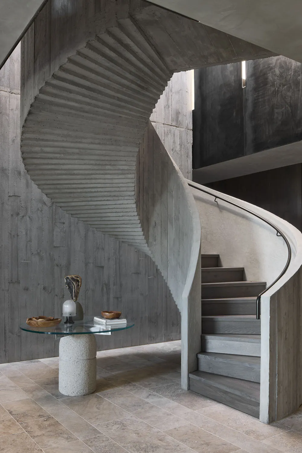 A modern interior design featuring a concrete staircase with a glass table in front.