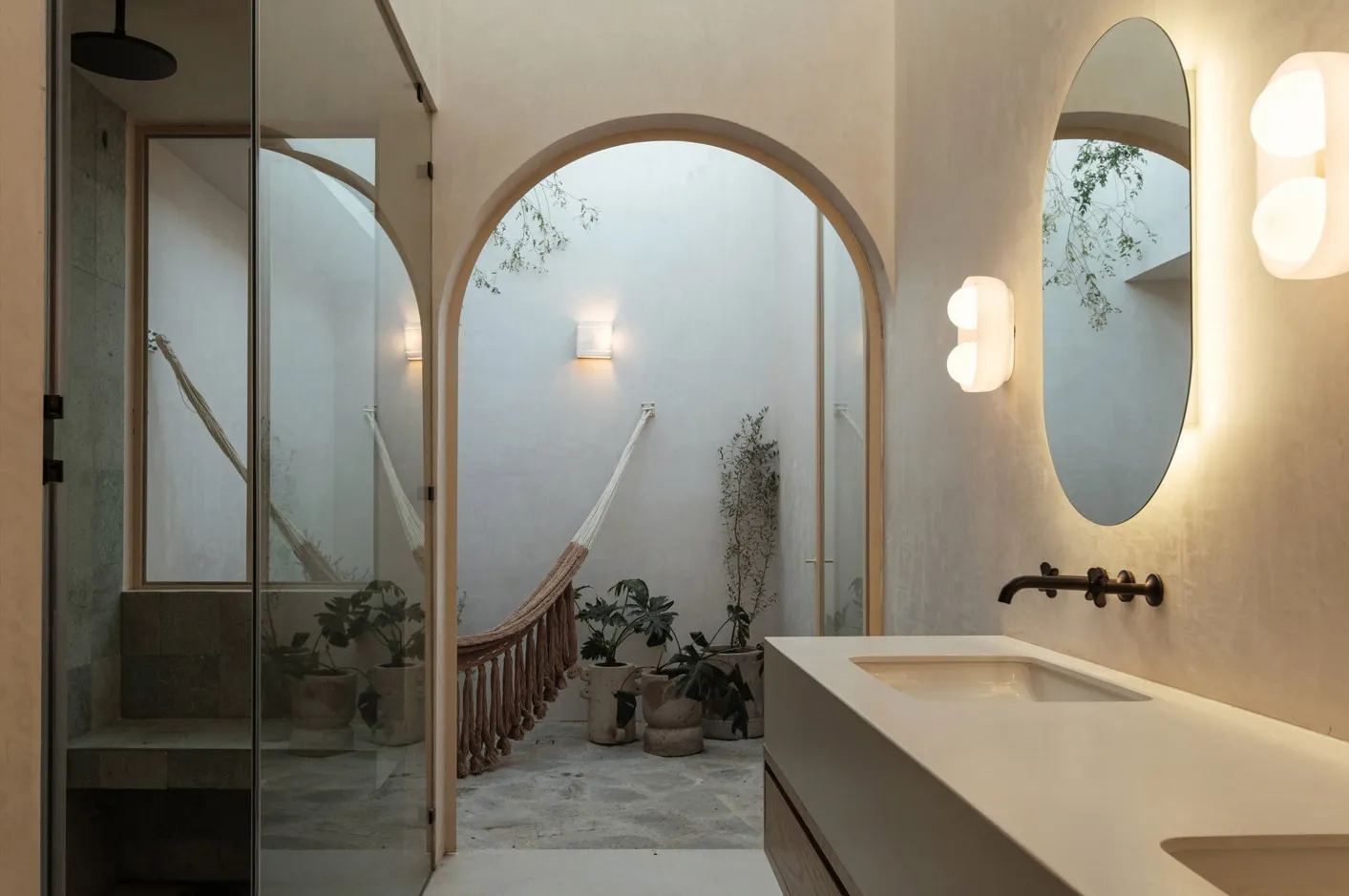 A minimalist bathroom with concrete walls, glass shower, and a garden view through an archway.