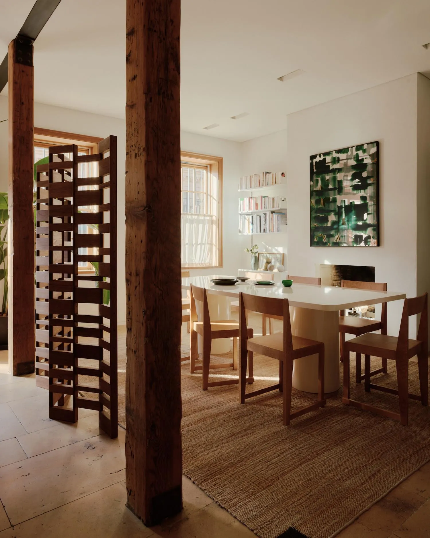 A modern minimalist dining room featuring a wooden table with metal legs, surrounded by wooden chairs, and a large painting o