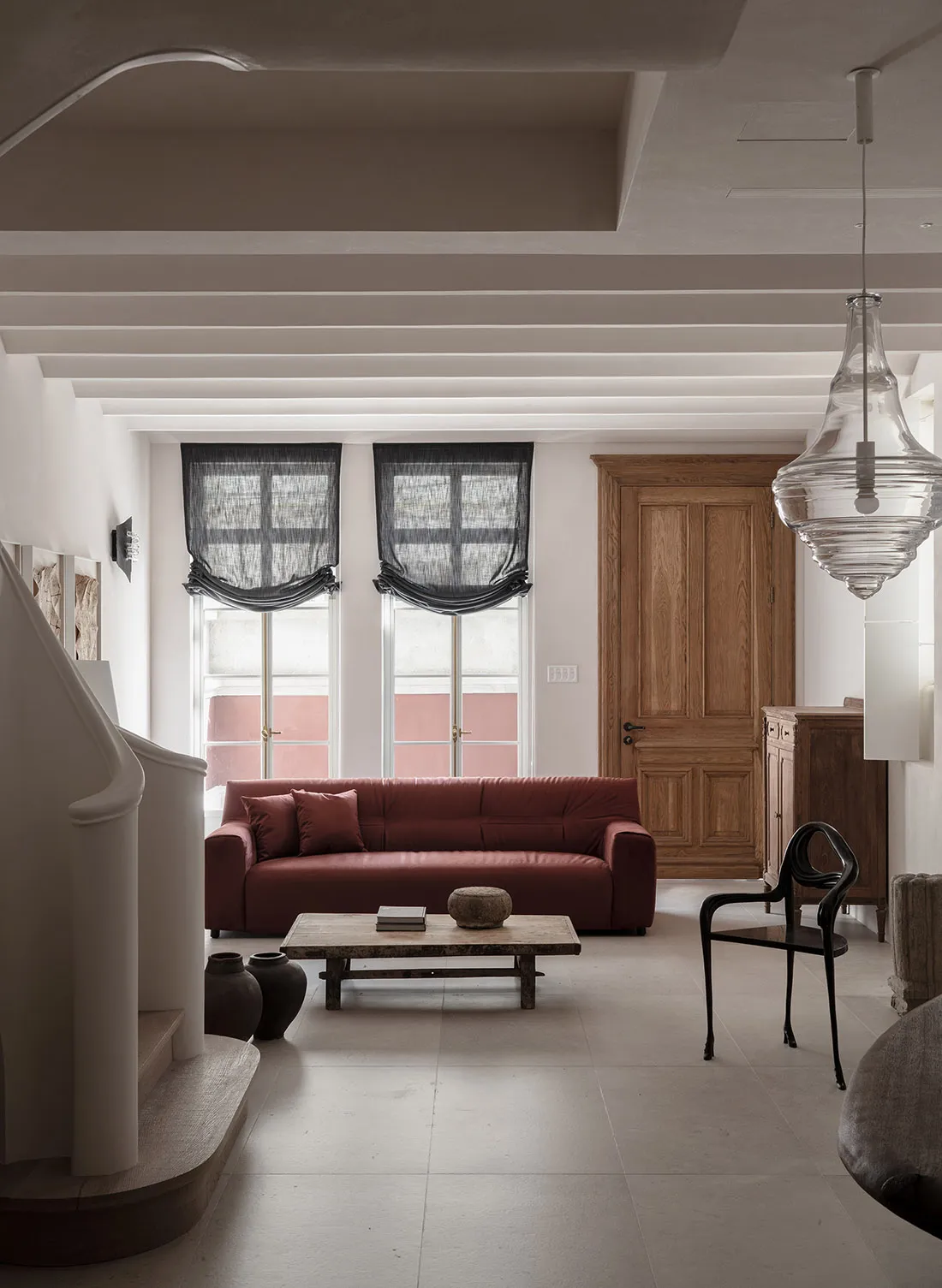 A minimalist living room with a red sofa, wooden coffee table, and black chairs.
