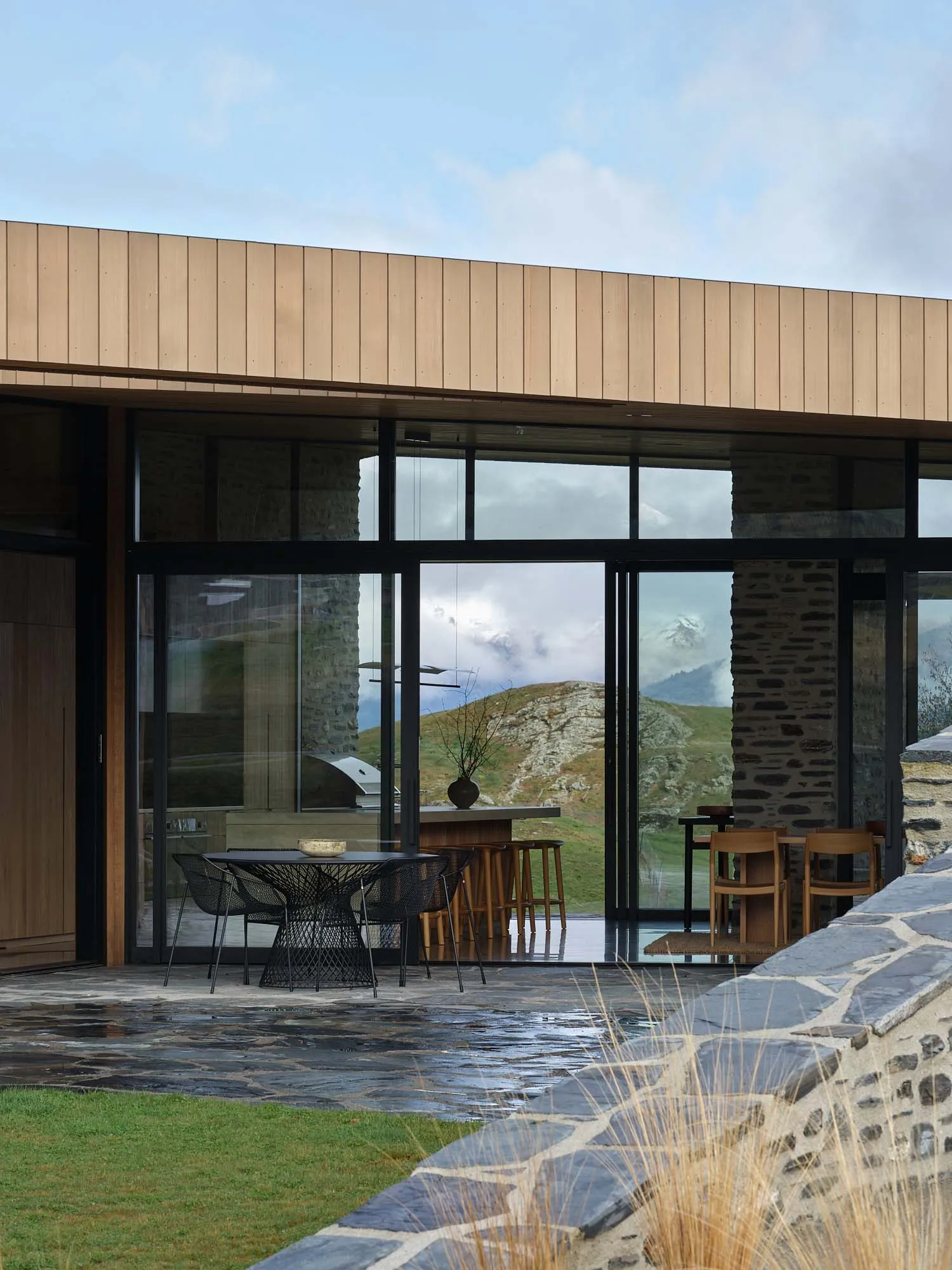 Modern residential interior featuring large glass windows, stone walls, and wooden elements.